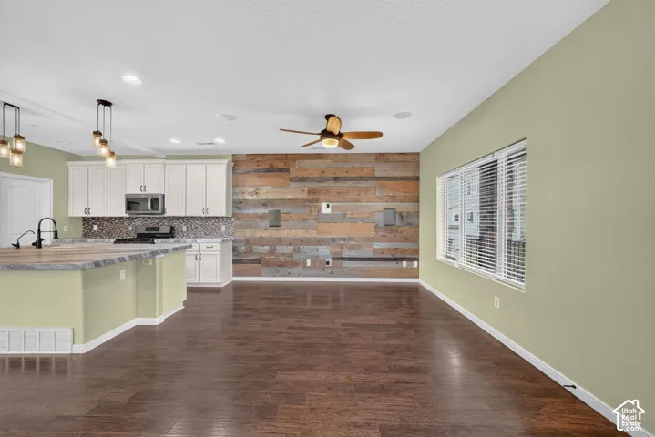 Open-concept interior featuring reclaimed wood accent wall, wood-finish flooring, white shaker-style cabinetry, multi-pendant lighting, and recessed ceiling fixtures
