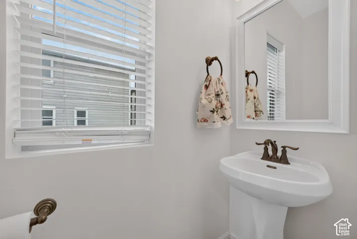 Pedestal sink with a dual-handle bronze faucet, framed wall mirror, and window with white horizontal blinds