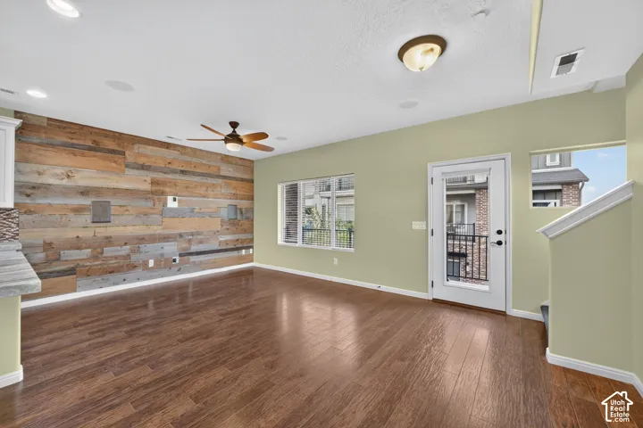 Wood-finish flooring, reclaimed wood-style accent wall, recessed lighting, ceiling fan, and glass-paneled exterior door
