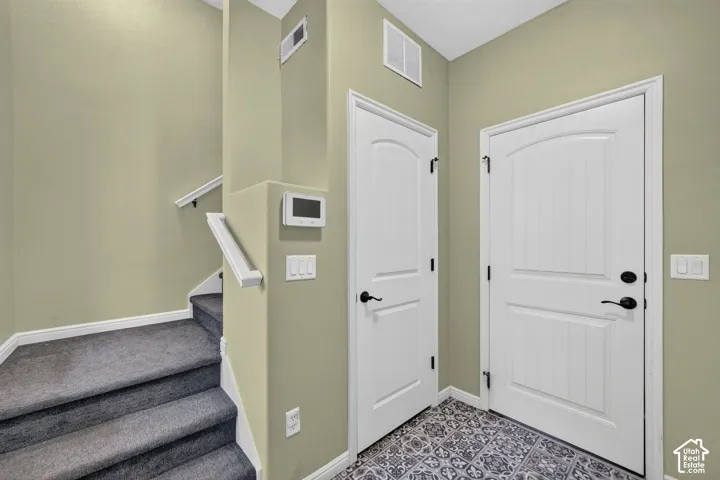 Entryway featuring patterned tile flooring, carpeted stairs with white handrails, arched-panel doors, and wall-mounted security system interface