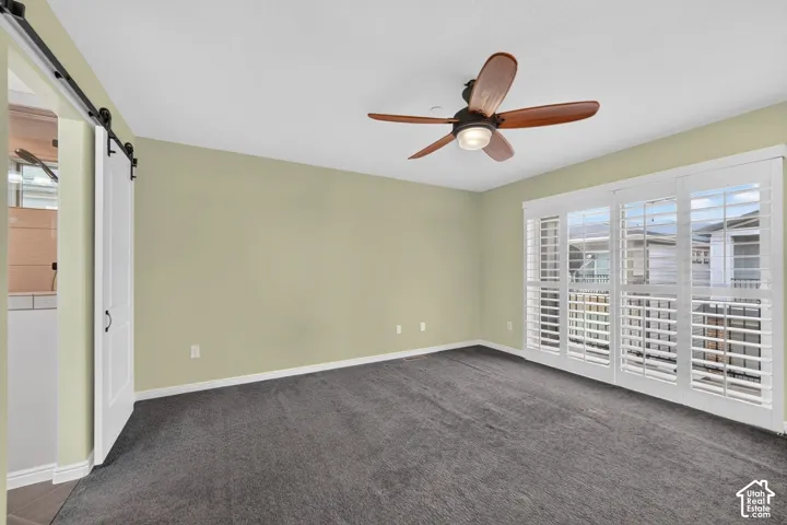 Primary featuring carpeted flooring, a ceiling fan with integrated lighting, a sliding white barn-style door, and large glass sliding doors with white plantation shutters
