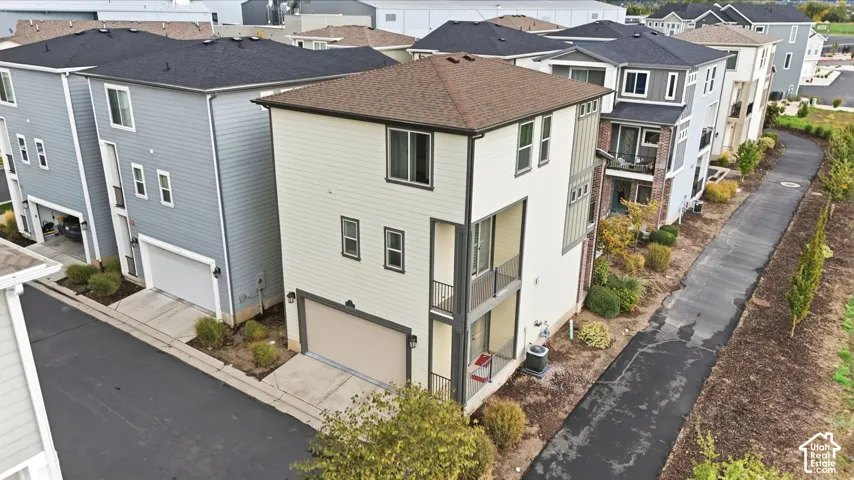 Three-story exterior featuring tan horizontal lap siding, a two-car garage, stacked private balconies with metal railings, and a hip roof with asphalt shingles