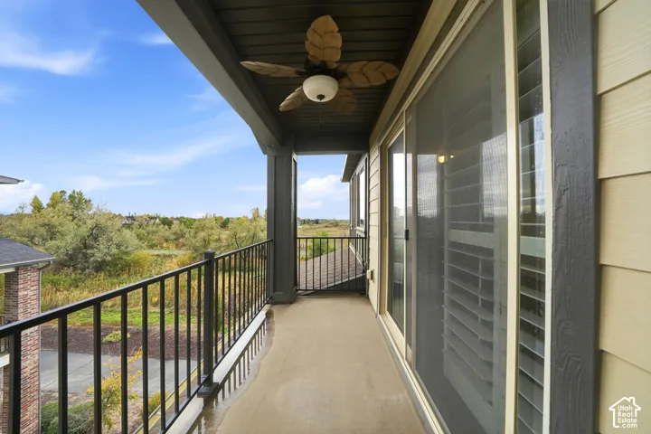 Covered balcony featuring black metal railing, concrete flooring, ceiling fan with palm-style blades, and sliding glass door