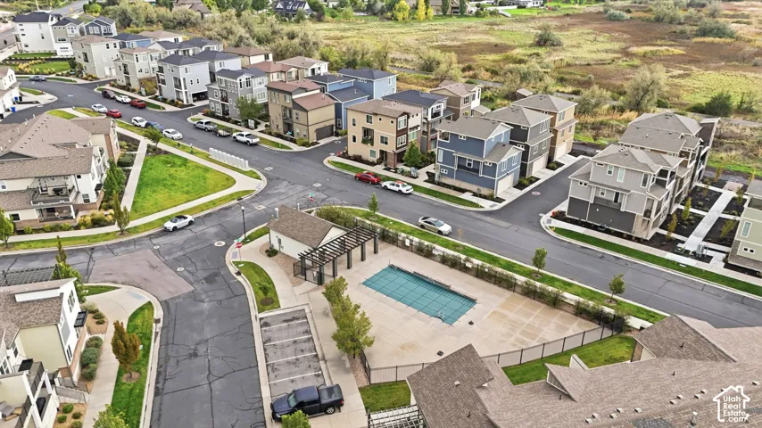 Aerial perspective of residential community featuring a fenced outdoor swimming pool, integrated pergola structure, and paved parking area