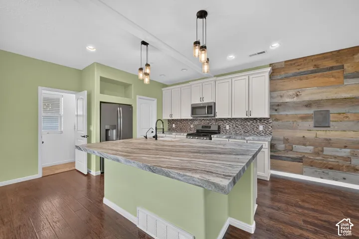 Kitchen featuring a large center island with a stone countertop, white cabinetry, wood-plank accent wall, mosaic tile backsplash, and recessed and pendant lighting