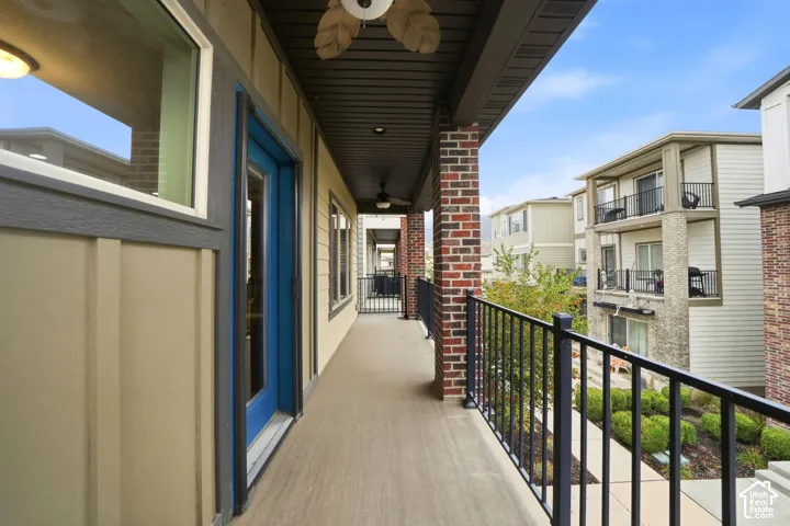 Covered exterior balcony featuring brick pillar accents, composite decking, black metal railing, and a ceiling-mounted fan