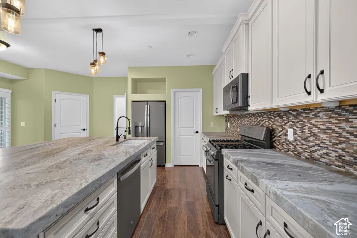 Kitchen featuring an oversized central island with stone-finish countertops, white shaker-style cabinetry, mosaic tile backsplash, wood-finish flooring, and pendant lighting