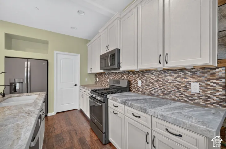 Kitchen featuring off-white cabinetry with dark hardware, stone-finish countertops, a mosaic tile backsplash, wood-finish flooring, and stainless steel appliances