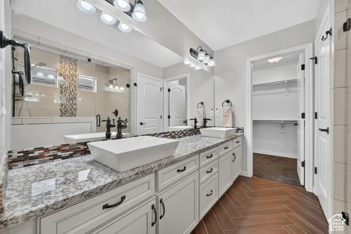 Primary Bath featuring a double vanity with rectangular vessel sinks, light-toned stone-finish countertops, herringbone-pattern wood-finish flooring, glass-enclosed shower with tiled accents, and Shaker-style cabinetry