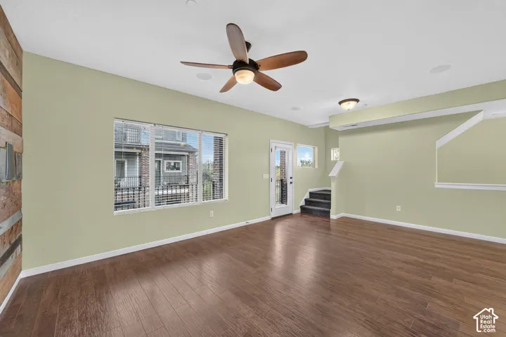 Wood-finish flooring, accent wall featuring reclaimed wood paneling, ceiling fan with integrated lighting, and multi-pane window