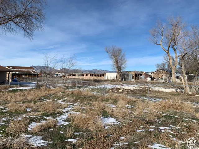 Expansive lot featuring mature trees, chain-link perimeter fencing, and mountain scenery