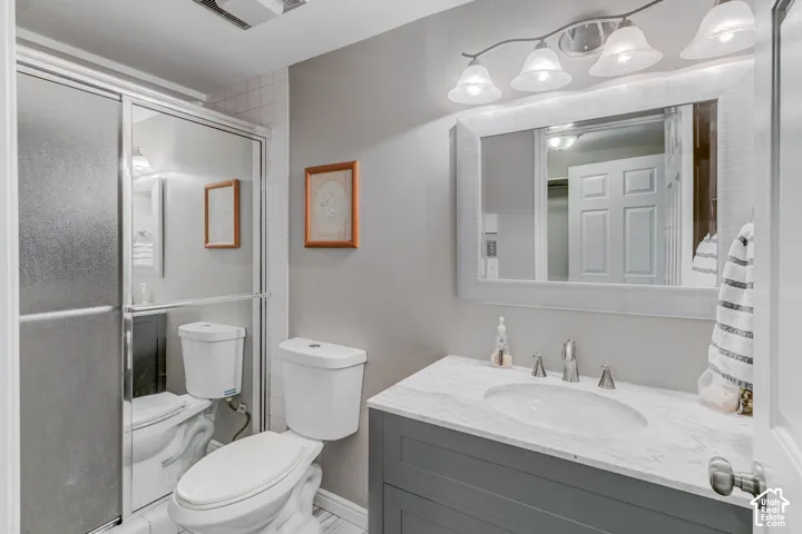 Bathroom featuring a gray vanity with a stone-top integrated sink, chrome widespread faucet, a framed mirror with a four-light fixture, and a glass-enclosed shower