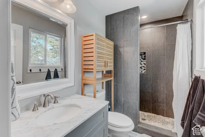 Bathroom vanity with stone-finish countertop, undermount sink, and brushed-nickel faucet, accompanied by a shower featuring dark vertical wall tile, stone pebble flooring, and a decorative mosaic inlay