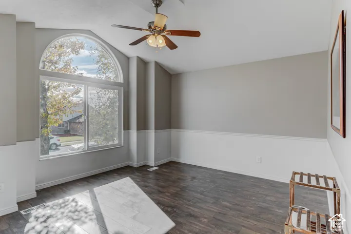 Vaulted ceiling featuring an arched window, wood-finish flooring, two-tone wall paint, and a ceiling fan with integrated lighting