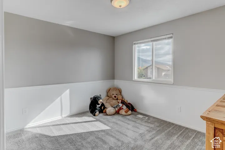 Neutral-toned walls featuring white wainscoting, grey carpeting, a double-pane sliding window, and a flush-mount overhead light fixture