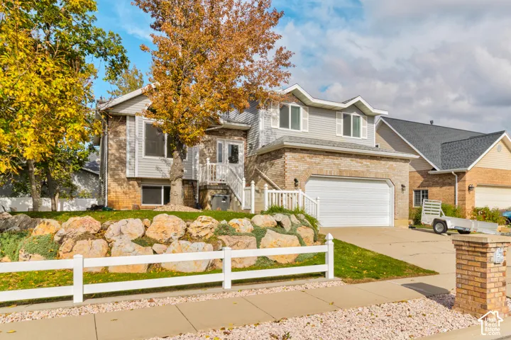 Two-story residence featuring a brick and horizontal siding exterior, attached two-car garage, terraced rock landscaping, and a white picket fence