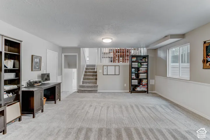 Neutral wall paint, plush carpeting, chair rail molding, ceiling-mounted light fixture, and stairs with white balusters