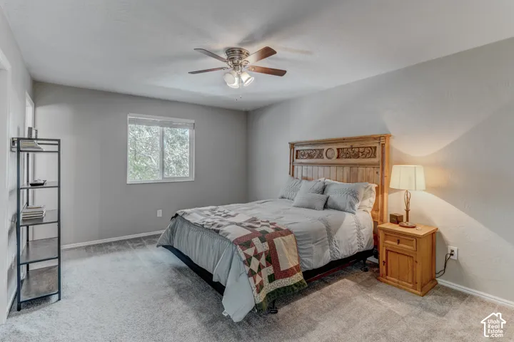 Neutral-toned bedroom featuring carpeting, a multi-blade ceiling fan with integrated lighting, and a window with horizontal blinds