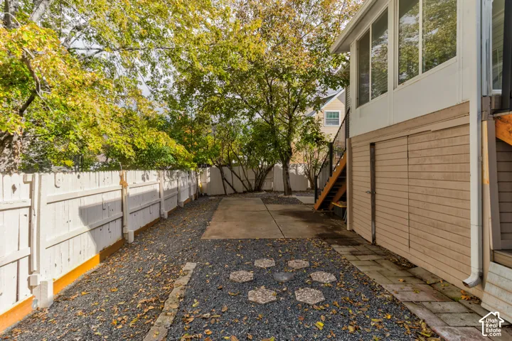 Enclosed side yard featuring white wood-style fencing, gravel landscaping, concrete slab, and built-in under-deck storage
