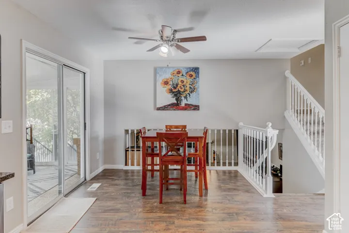 Wood-finish flooring, sliding glass door, ceiling fan with integrated light fixture, and white painted wooden stair railing