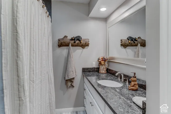 Vanity with dark stone countertop, undermount sink, white cabinetry, integrated mirror, and recessed lighting
