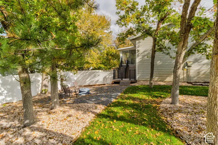 Backyard featuring a vinyl privacy fence, stone ground cover, mature trees, and an elevated exterior deck with stairs and metal railings