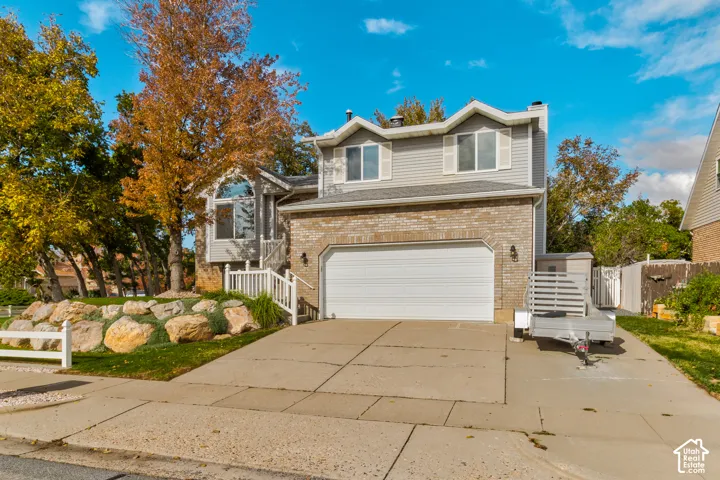 Split-level exterior featuring a brick and horizontal siding facade, two-car garage, and terraced landscaping with natural stone retaining walls