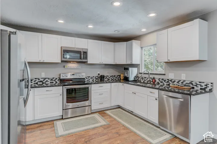 Kitchen featuring white cabinetry, stainless steel appliances, dark stone-finish countertops, multi-toned mosaic backsplash, and recessed lighting