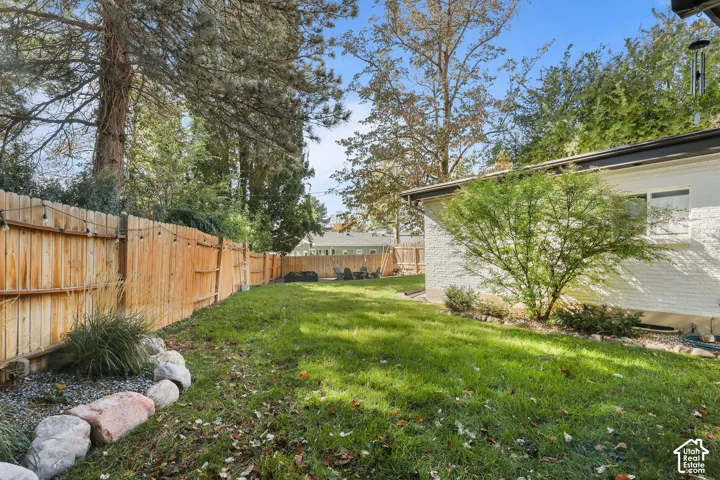 Backyard space featuring a grass lawn, natural stone edging, perimeter wood fencing, and mature trees