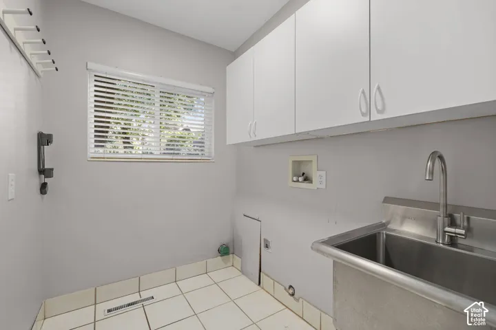 Utility room featuring white cabinetry, a stainless steel utility sink with a high-arch faucet, wall-mounted storage rack, and tiled flooring