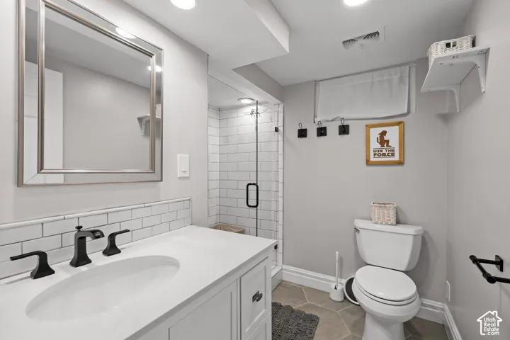 Bathroom featuring a white vanity with a composite countertop, subway tile backsplash, matte black widespread faucet, and a glass-enclosed shower with subway tile surround