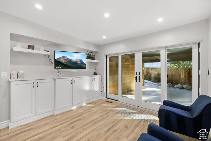 Living area featuring wood-finish flooring, recessed lighting, built-in white cabinetry with countertop surfacing, floating wall shelves, and sliding glass doors
