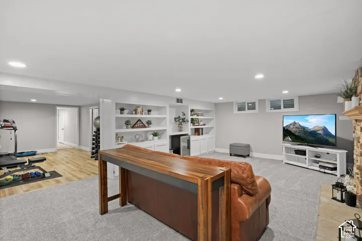 Open concept space featuring recessed lighting, custom white built-in shelving, wood-finish flooring, wall-to-wall carpeting, and a stone-clad hearth
