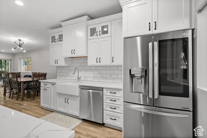 Kitchen featuring white cabinetry, subway tile backsplash, white farmhouse-style sink, quartz countertops, and stainless steel appliances