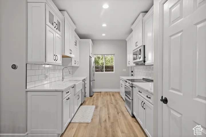Kitchen featuring white shaker-style cabinetry, white subway tile backsplash, farmhouse sink, stainless steel appliances, and wood-finish flooring