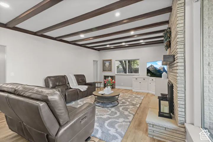 Living area featuring wood-finish flooring, exposed ceiling beams, recessed lighting, and a floor-to-ceiling masonry fireplace with a raised hearth
