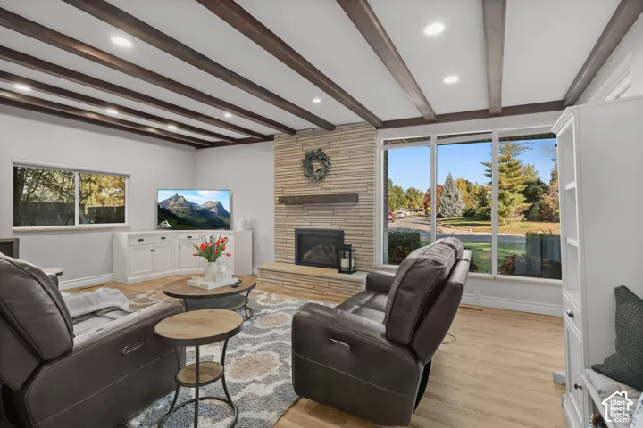 Exposed wood ceiling beams, floor-to-ceiling stacked stone fireplace with a timber mantel, large picture windows, wood-finish flooring, and built-in cabinetry