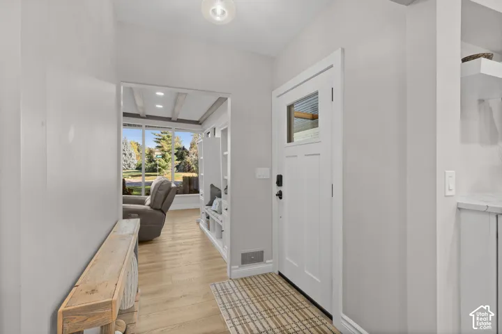 Entryway featuring a white door with a glass inlay, light wood-finish flooring, built-in shelving, and a modern overhead light fixture