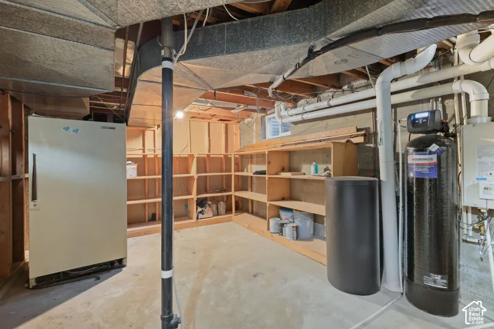 Utility area featuring built-in wooden shelving, a water filtration system, concrete flooring, and exposed ductwork