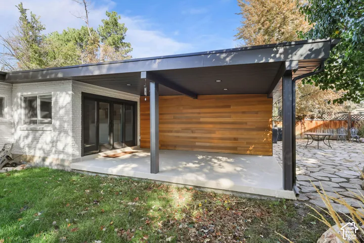 Covered patio featuring wood-paneled accent wall, concrete flooring, recessed lighting, and steel support beams, complemented by an expansive flagstone hardscape