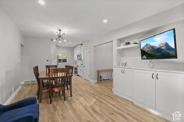 Wood-finish flooring throughout with built-in cabinetry featuring white shaker-style doors, recessed lighting, a modern multi-arm chandelier, and a custom recessed wall niche with stone countertop and integrated shelf