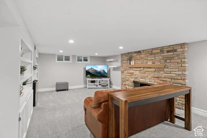 Full-height stone fireplace with a wood mantel, recessed lighting, built-in shelving, and carpeted flooring