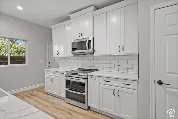 Kitchen featuring white shaker-style cabinetry, stainless steel appliances, subway tile backsplash, light stone-finish countertops, and wood-finish flooring