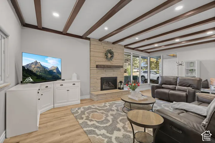 Living area featuring exposed wood ceiling beams, floor-to-ceiling horizontal stone fireplace surround, wood-finish flooring, and expansive windows
