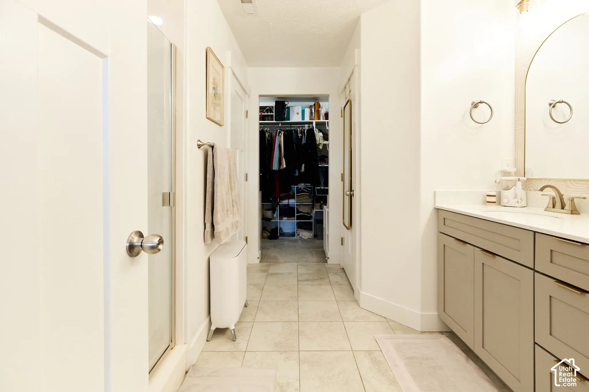 Bathroom featuring a light-toned vanity with cabinet storage, arched mirror, tiled flooring, and a glass-enclosed shower