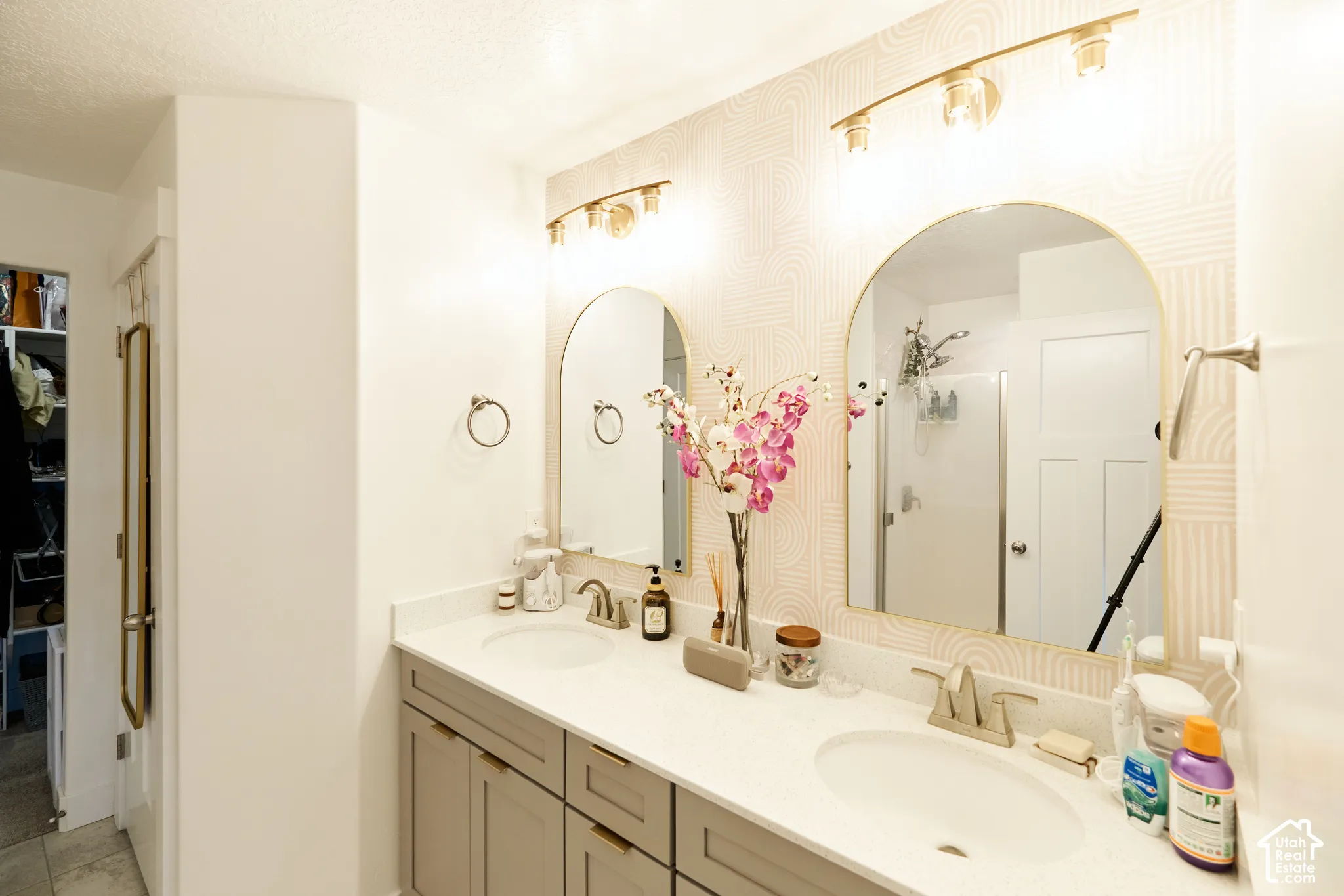 Dual-sink vanity featuring grey cabinetry, solid-surface countertops, twin arched mirrors, and two three-light vanity fixtures