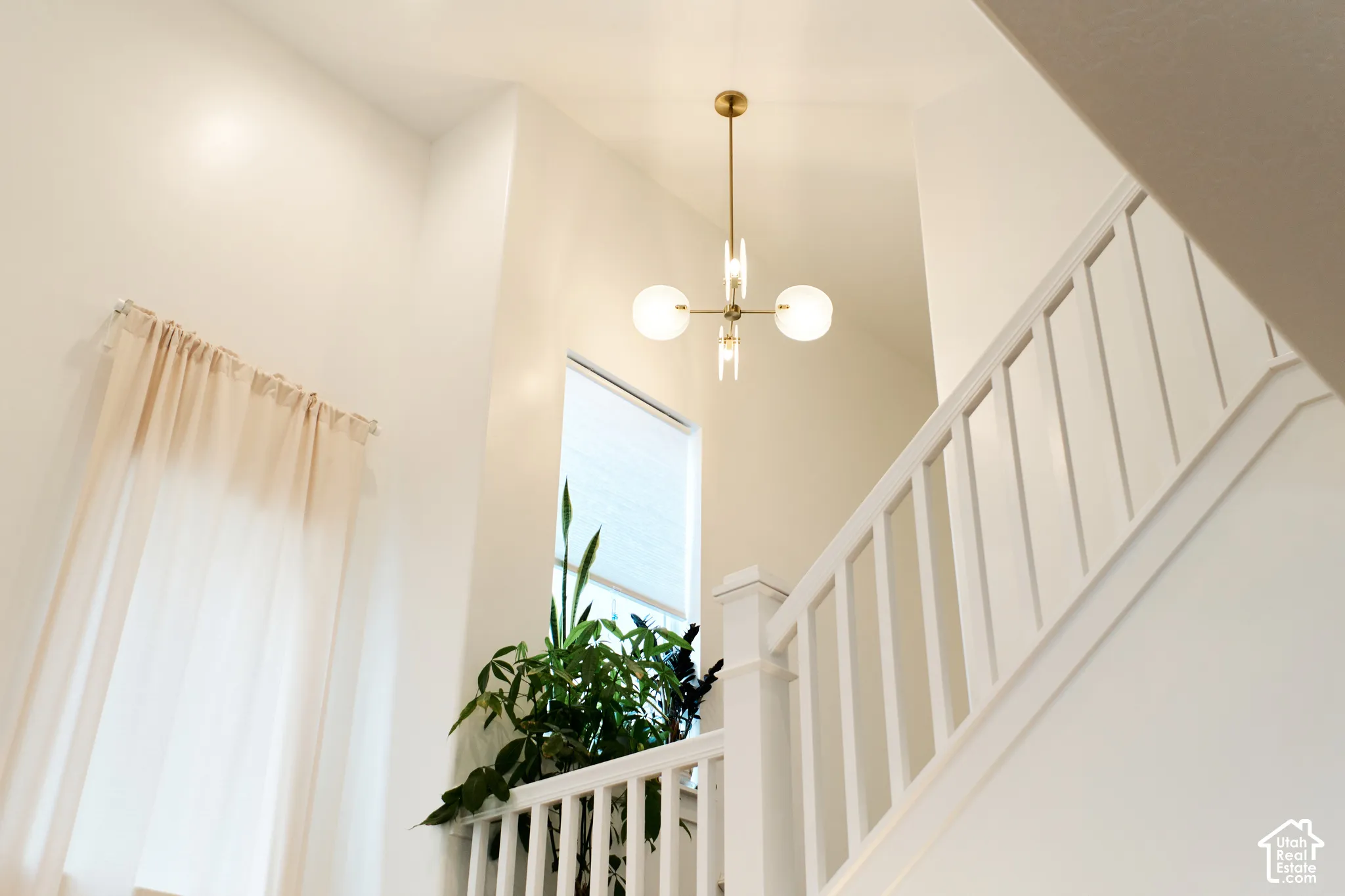 Vaulted ceiling featuring a brass multi-globe pendant chandelier, white-painted wood railing, and vertical window