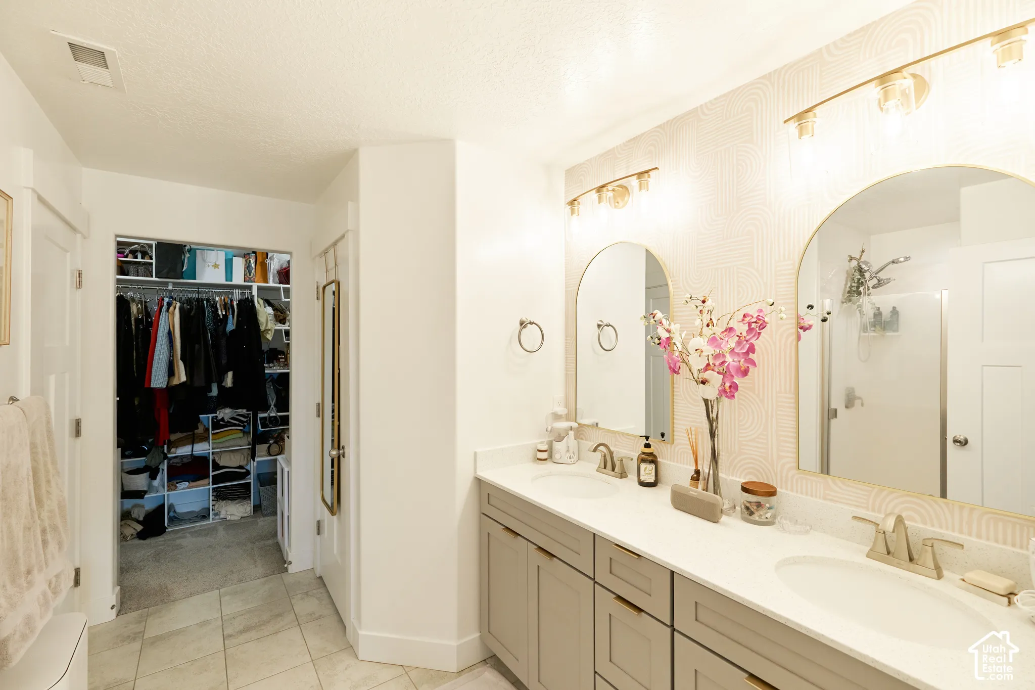 Dual-sink vanity with light-tone cabinetry, stone-finish countertops, arched mirrors, and integrated storage