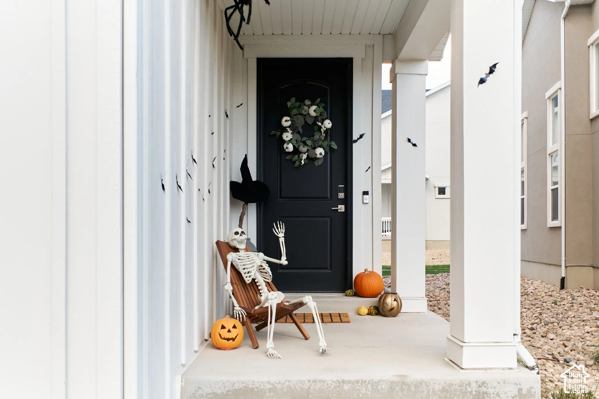 Covered front porch featuring vertical board-and-batten siding, a solid core entry door with an arched glass inset, and a concrete landing supported by a square architectural pillar