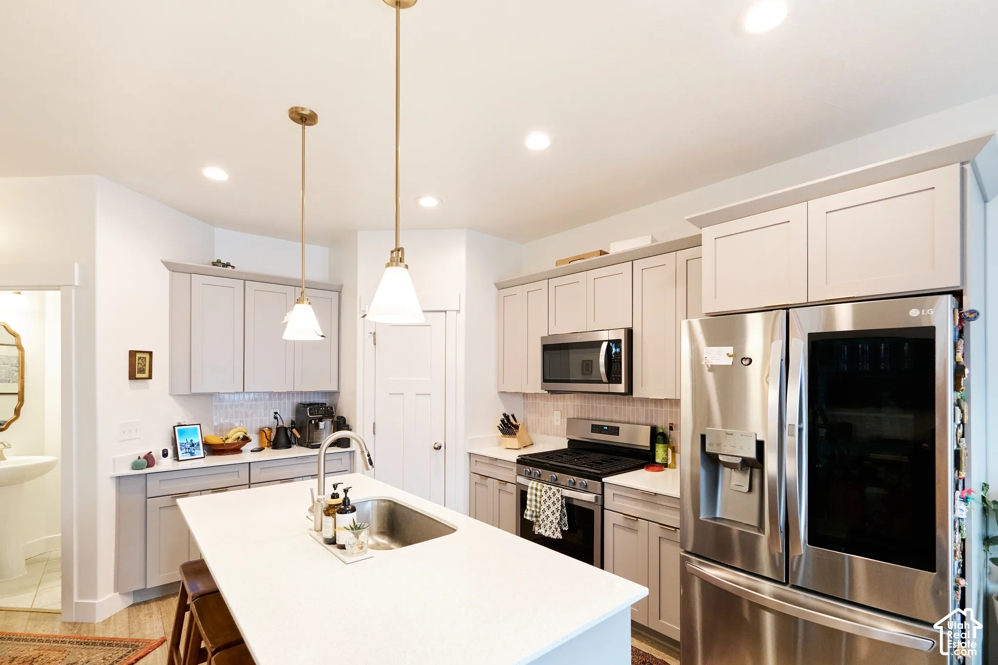 Kitchen featuring shaker-style cabinetry, a central island with an undermount sink, quartz countertops, stainless steel appliances, and pendant lighting